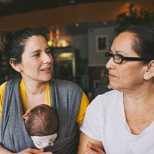 Mutter mit Baby in der Trage unterhält sich mit einer älteren Frau Mutter mit Baby in der Trage unterhält sich mit einer älteren Frau