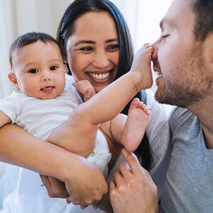 Die Mutter hält das Baby und lächelt. Das Baby hat einen Fuß auf der Nase des Vaters. Die Mutter hält das Baby und lächelt. Das Baby hat einen Fuß auf der Nase des Vaters.